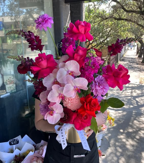 Pink and red armful with orchids, held outside the Norton St shop