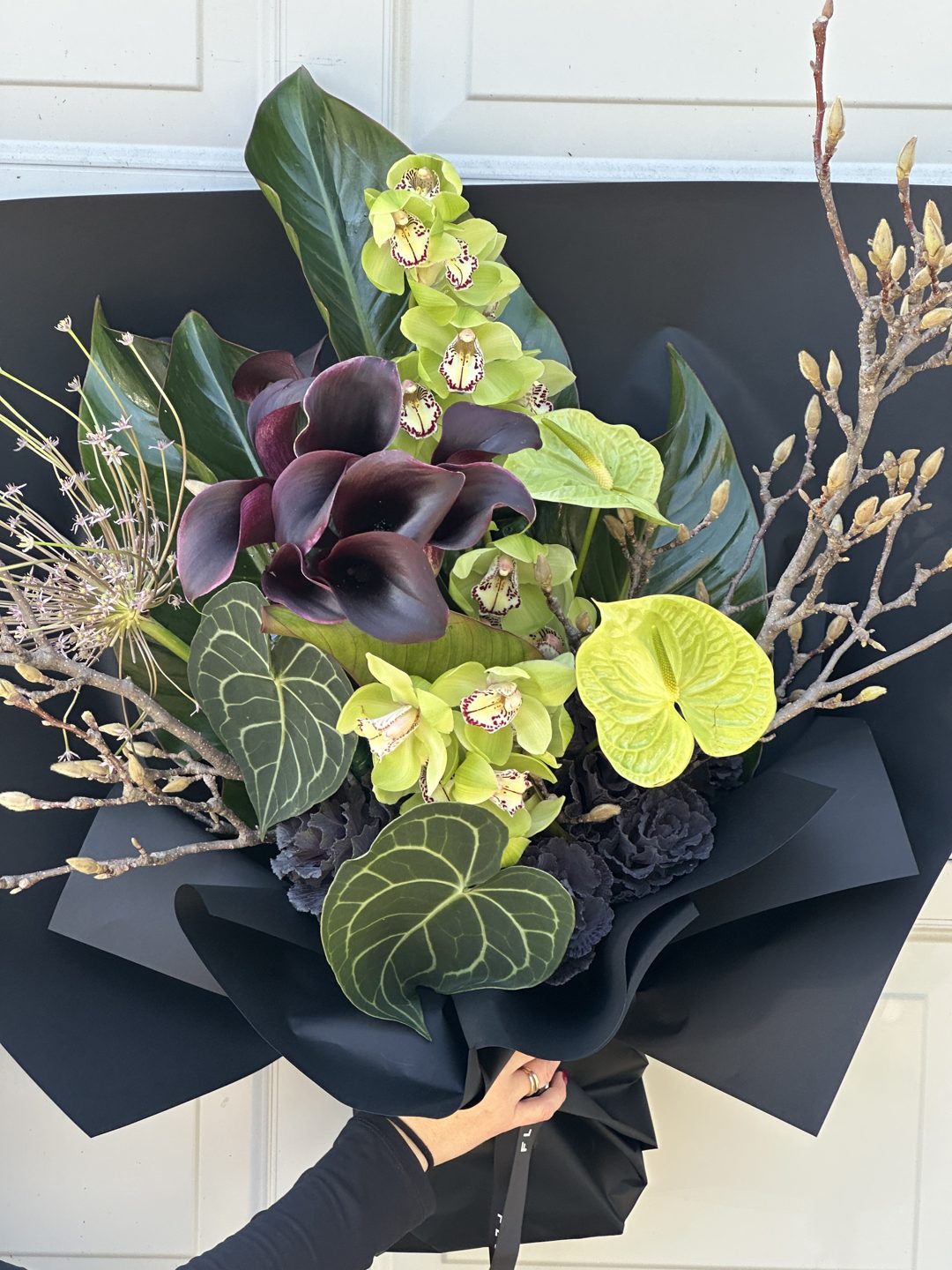 Green orchids and dark callas in a black wrap
