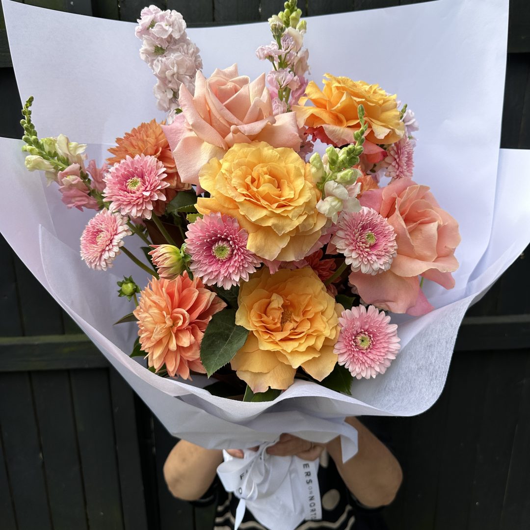 Peach roses and gerberas in a white wrap, held up in front of a face