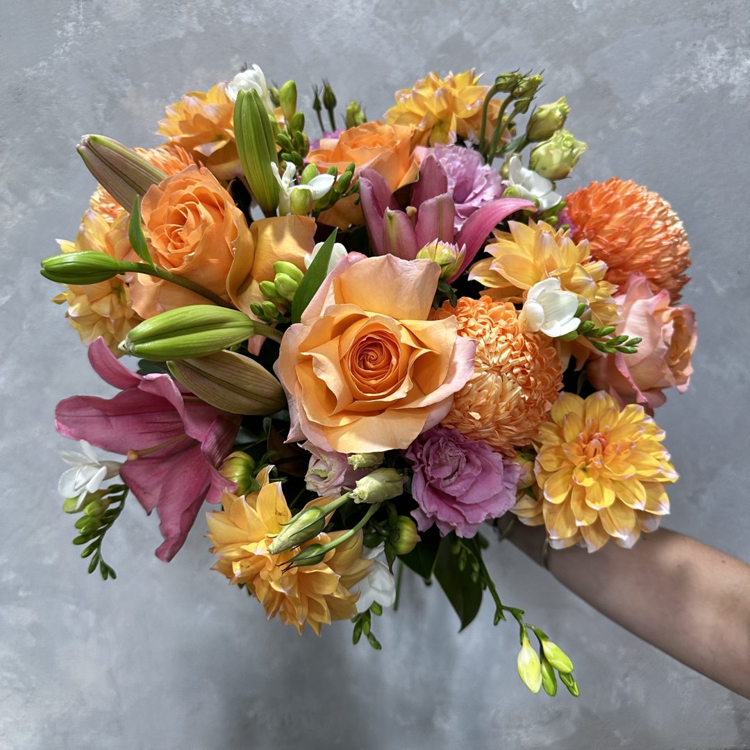 Orange roses, dahlias and lilies held in a hand
